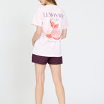 Person wearing a white t-shirt with a graphic design and purple shorts on a white background