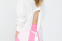 A person wearing a white long sleeve backless shirt paired with pink pants.