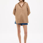 Woman wearing Mara Oversized Long Sleeve Shirt - Toffee in a relaxed fit paired with denim shorts and sandals