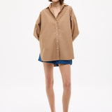 Woman wearing Mara Oversized Long Sleeve Shirt - Toffee in a relaxed fit paired with denim shorts and sandals