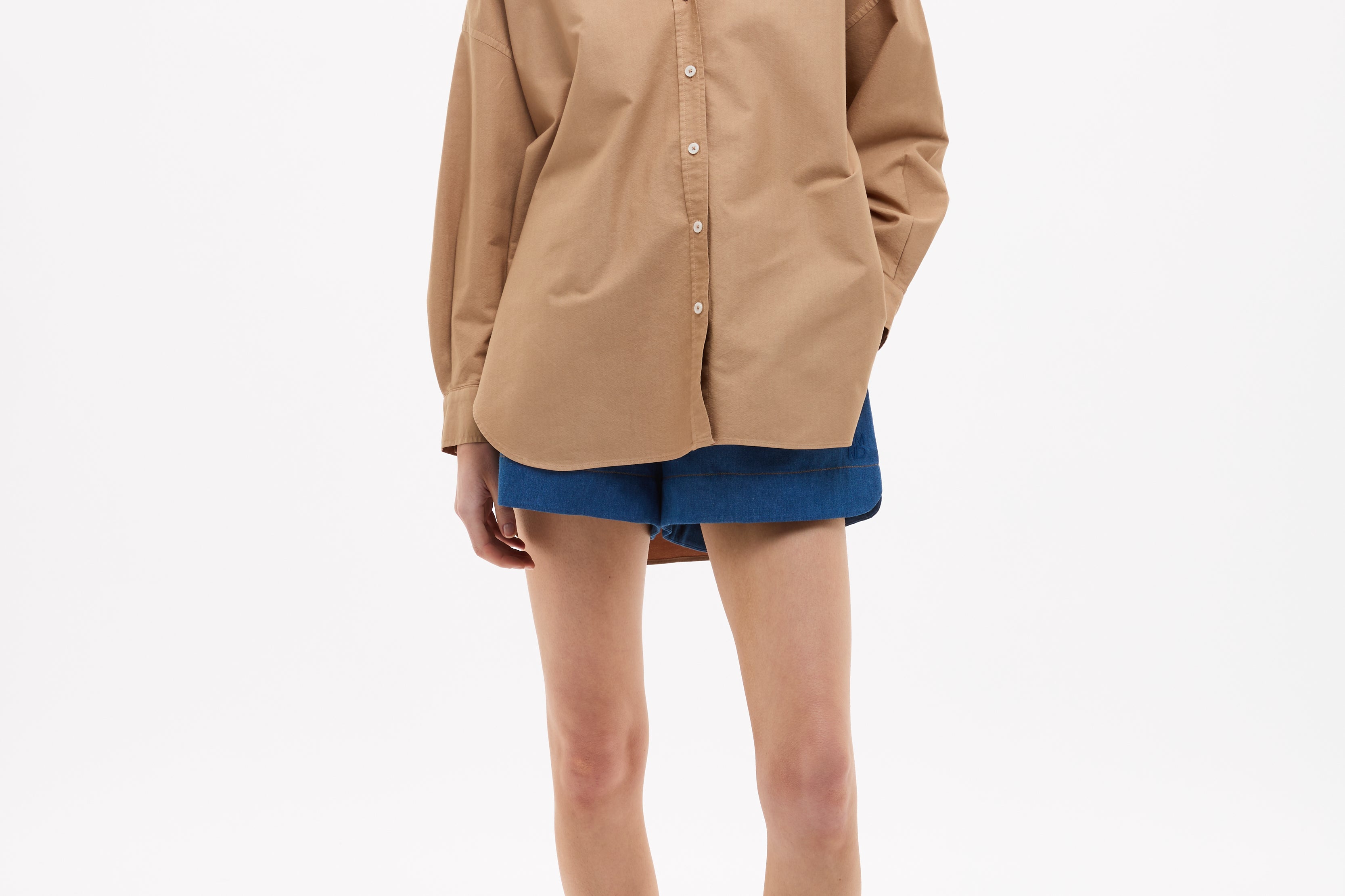 Woman wearing Mara Oversized Long Sleeve Shirt - Toffee with blue shorts and sandals against white background