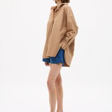 Woman wearing Mara Oversized Long Sleeve Shirt - Toffee with blue shorts and sandals, standing against white background