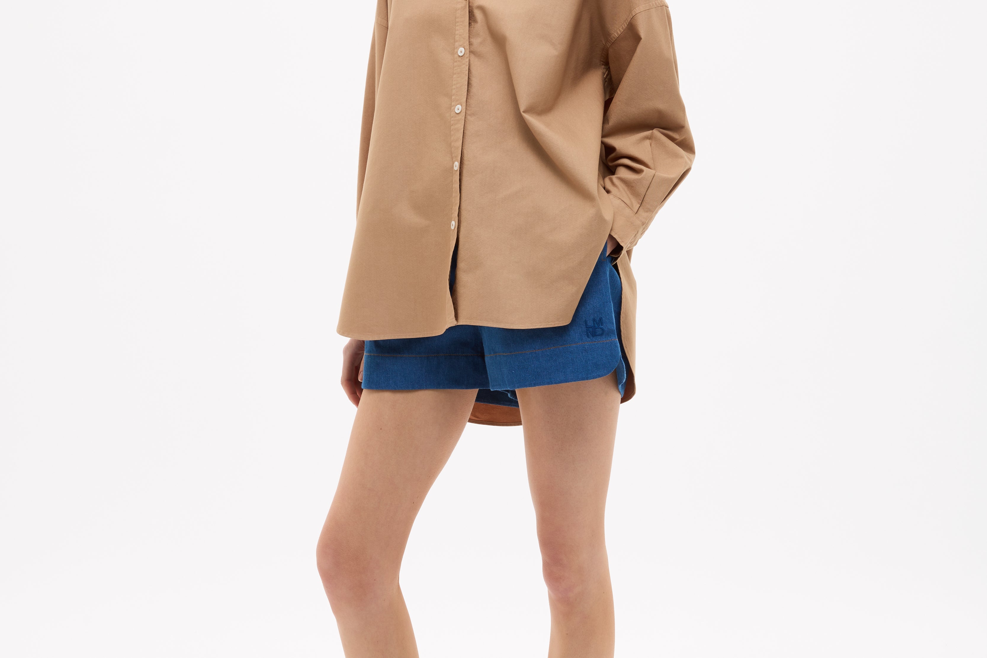 Woman wearing Mara Oversized Long Sleeve Shirt - Toffee with blue shorts and sandals against white background