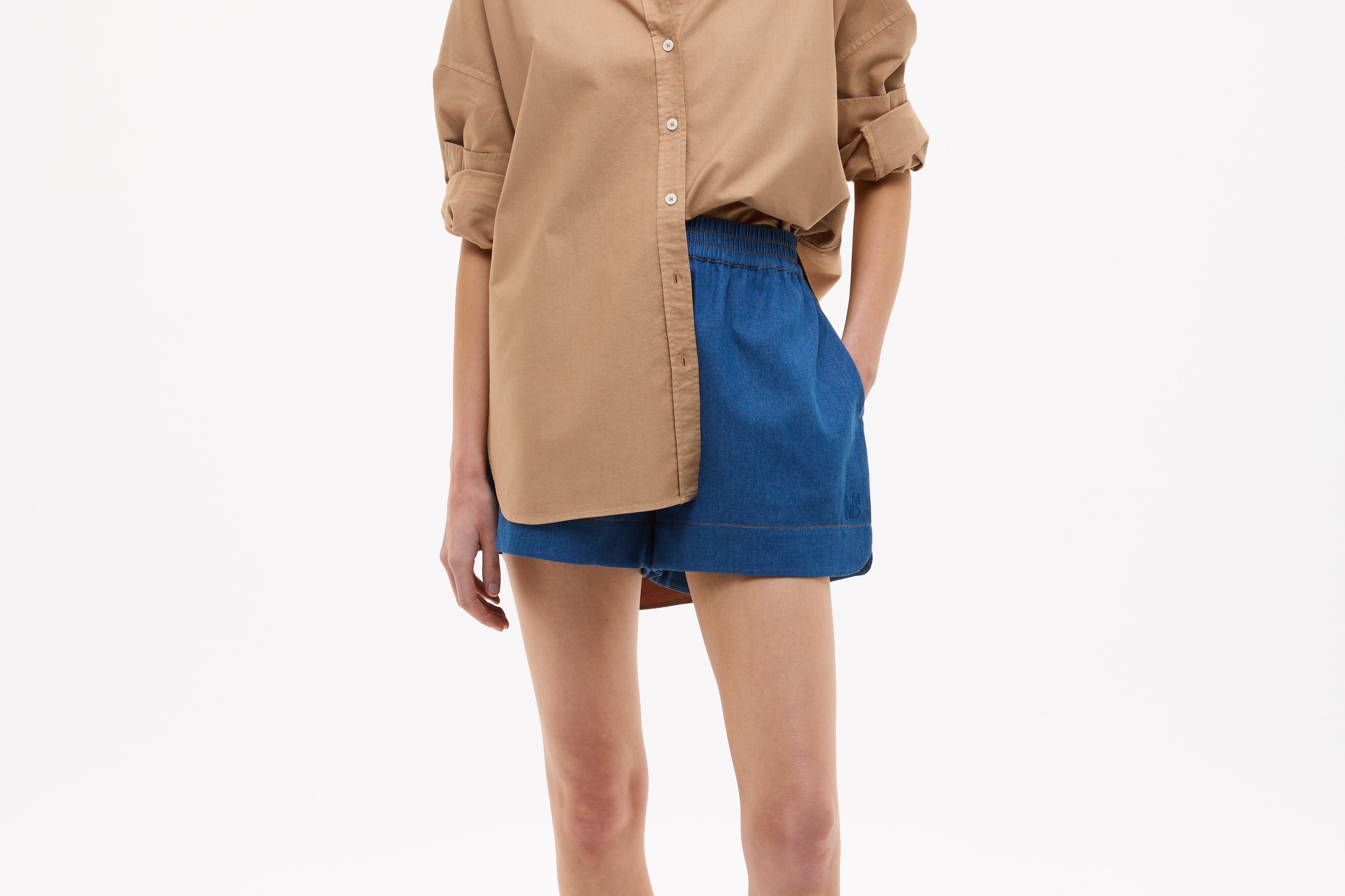 Woman wearing Mara Oversized Long Sleeve Shirt - Toffee with rolled-up sleeves paired with blue shorts and sandals
