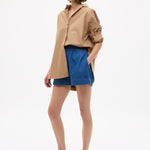 Woman wearing Mara Oversized Long Sleeve Shirt - Toffee with rolled sleeves paired with blue shorts and sandals