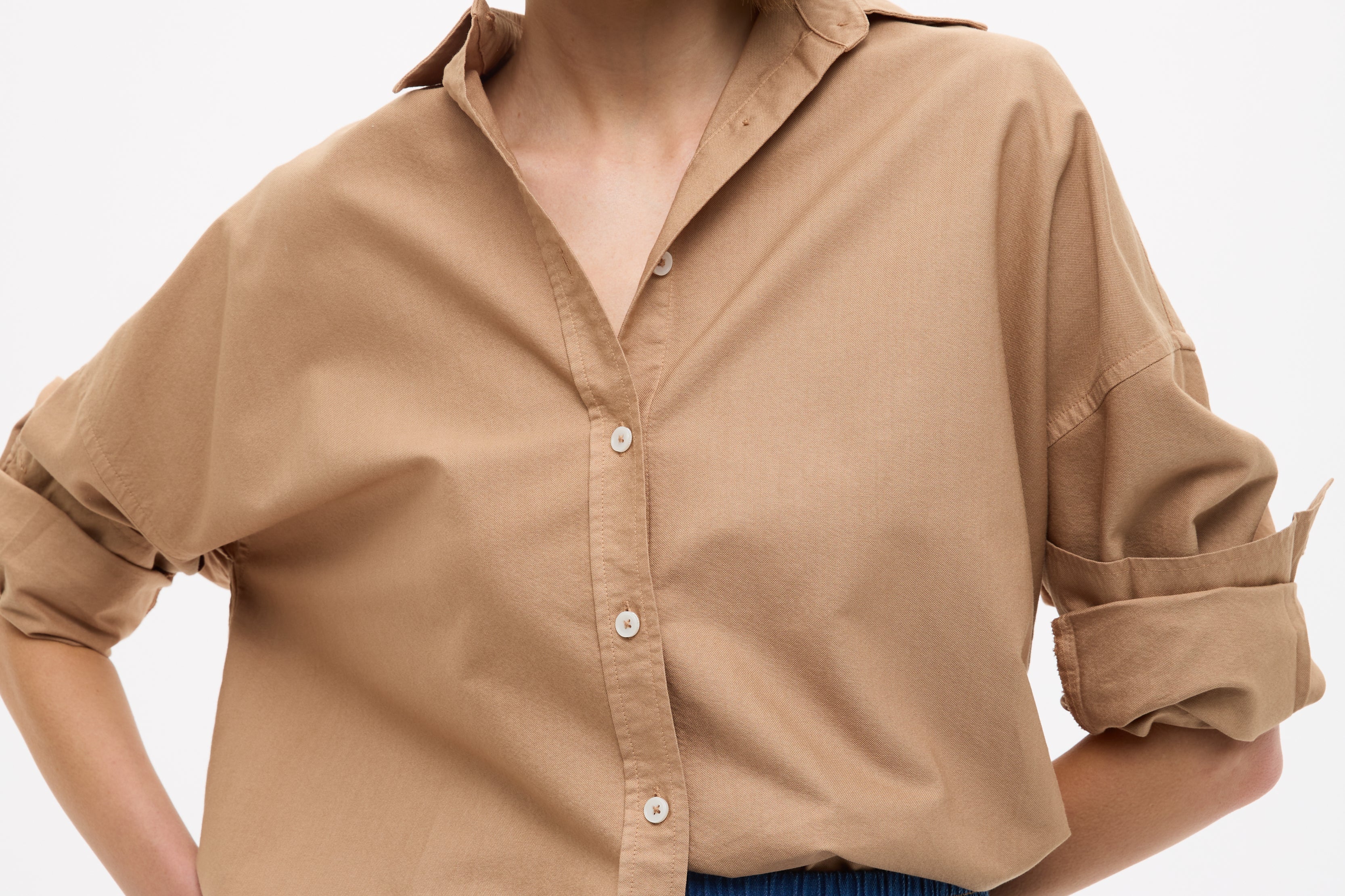Woman wearing Mara Oversized Long Sleeve Shirt - Toffee with rolled sleeves paired with blue casual pants against white background