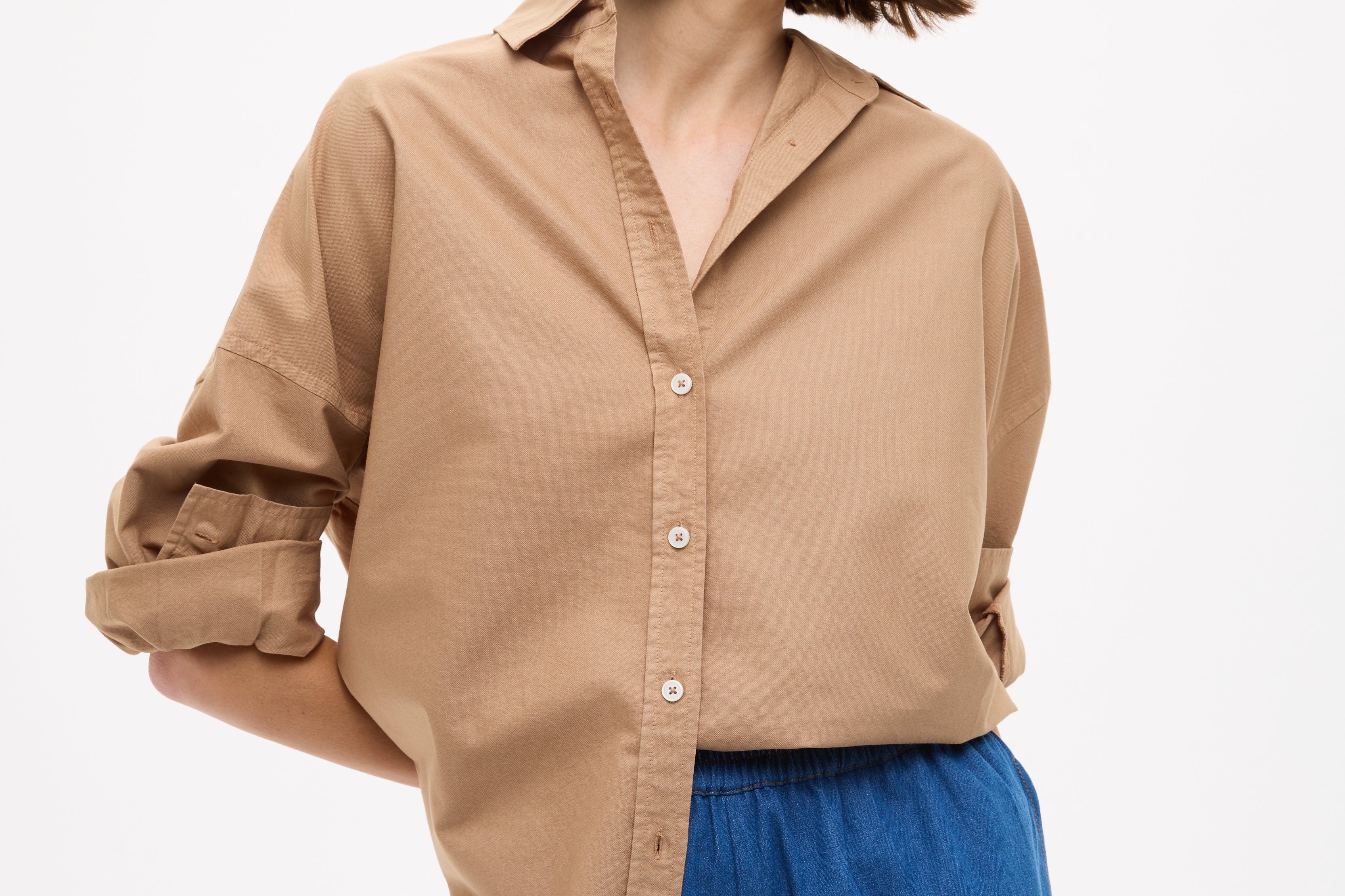 Woman wearing Mara Oversized Long Sleeve Shirt - Toffee tucked into casual blue high-waisted shorts, looking sideways