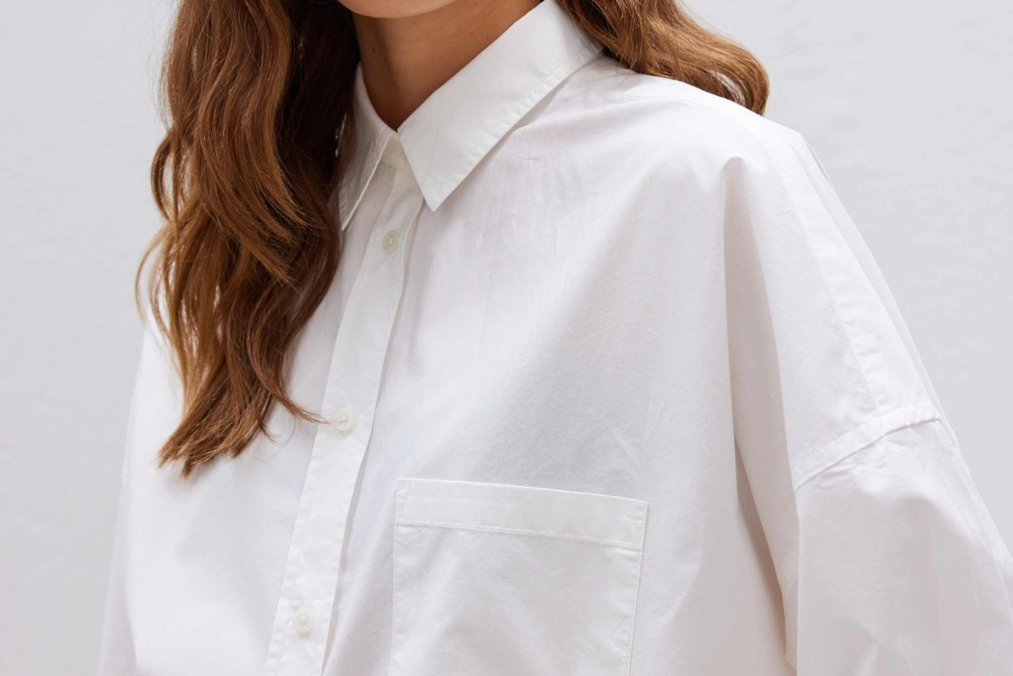 Woman wearing a relaxed fit white long sleeve shirt made from 100% organic cotton with custom buttons and curved hem