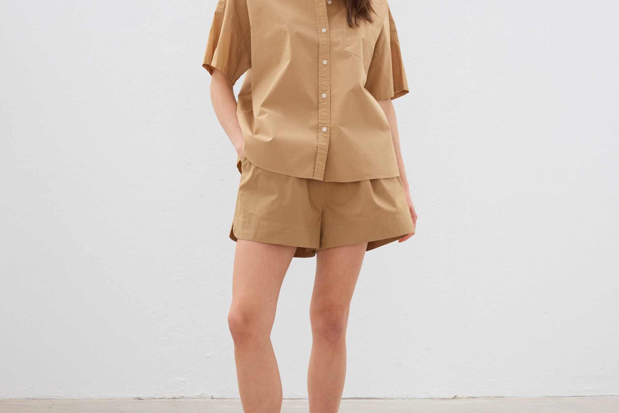 Woman wearing toffee cotton button-up short sleeve shirt and matching shorts with white sneakers