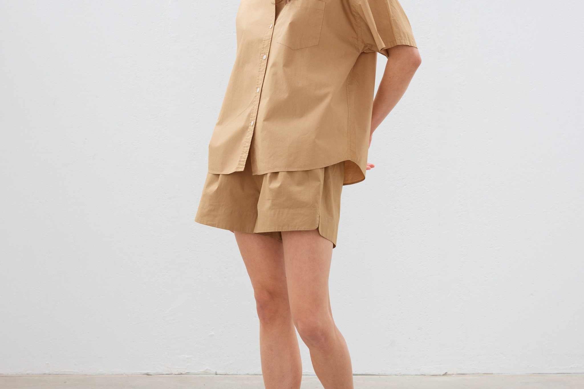 Woman wearing toffee color cotton button-up short sleeve shirt and matching shorts with white sneakers