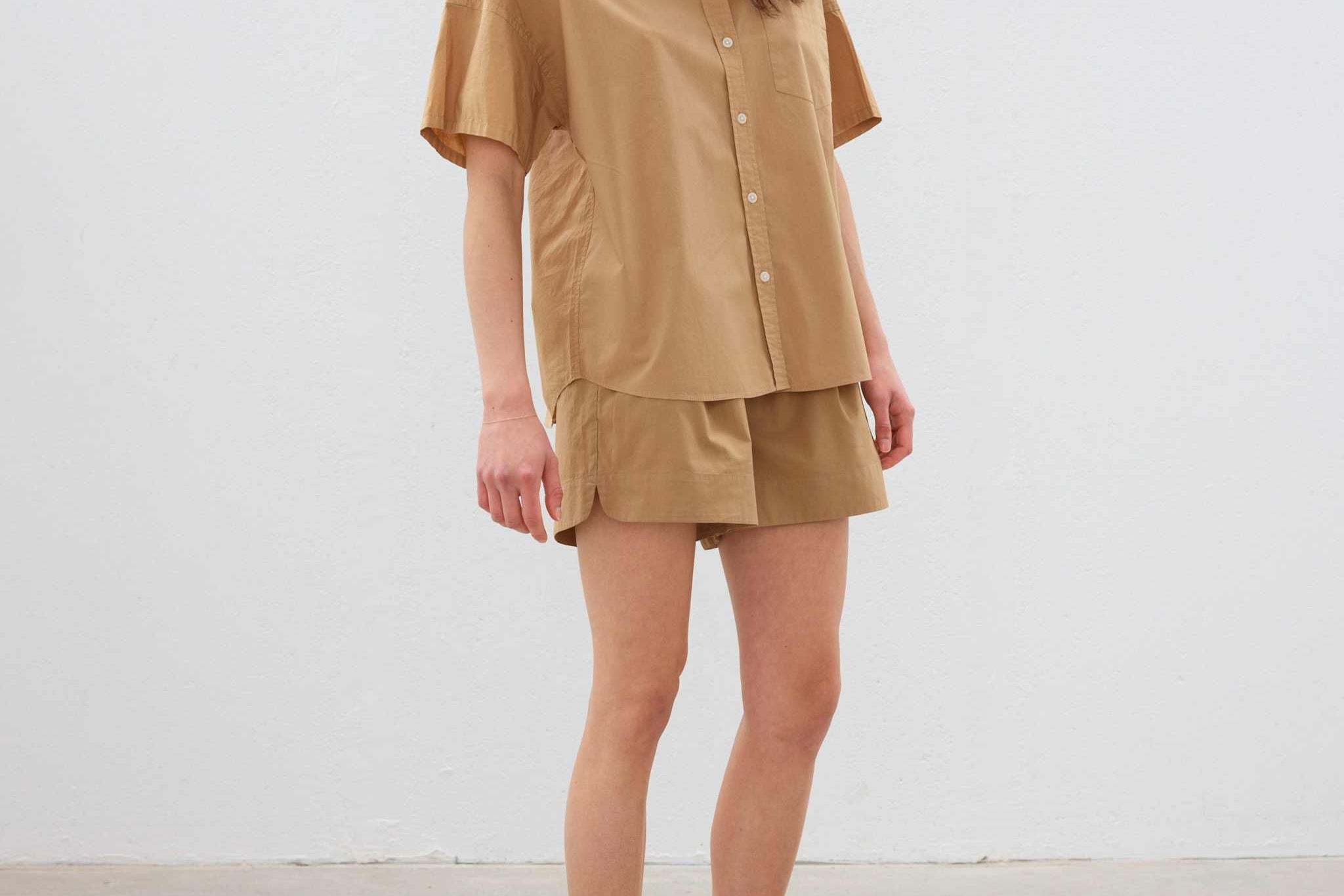 Woman wearing toffee color cotton button-up short sleeve shirt with matching shorts and white sneakers