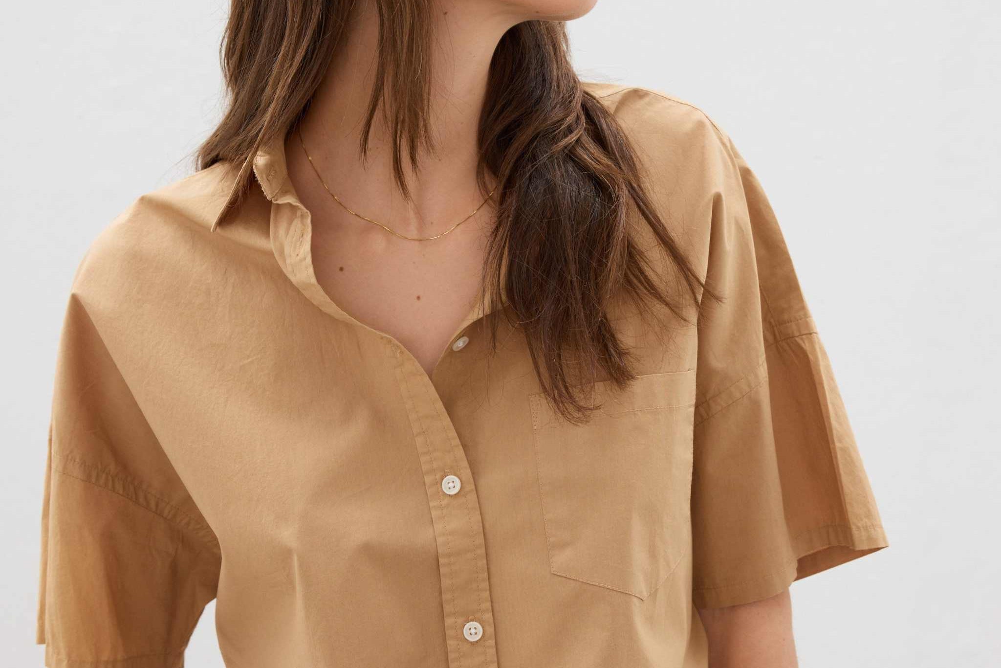 Woman wearing toffee-colored cotton button-up short sleeve shirt with relaxed fit and chest pocket